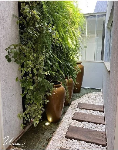 Jardim vertical e passarela de madeira ao lado de uma parede clara.