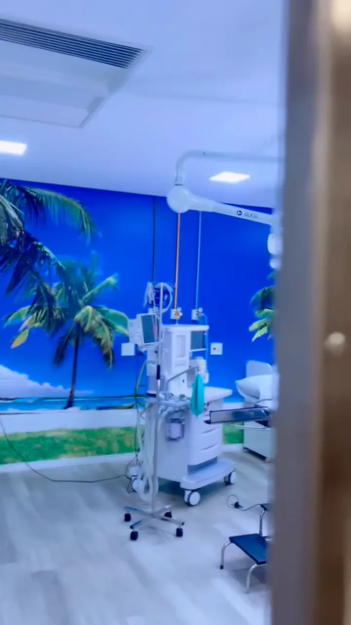 Sala cirúrgica com painel de praia e coqueiros na parede.