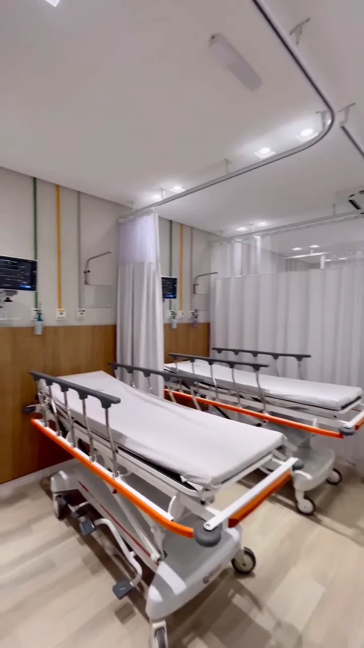 Sala de observação com macas, cortinas e painel de madeira.